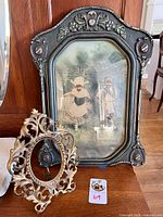 Photo showing two vintage decorative picture frames: a large black Victorian style frame with floral reliefs and a smaller ornate gold Rococo style frame in front.