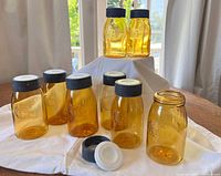 Eight amber glass jars with black metal lids displayed on a white cloth near window light.