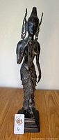Front view of vintage Thai bronze Buddha statue showing intricate details and statue's full height on wooden surface with lot number tag.