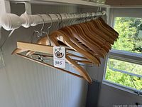 13 natural wooden hangers with metal hooks and 3 with crossbars on a white rack near window