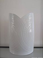 Front view of white porcelain vase showing intricate embossed line pattern and curved V shape top.
