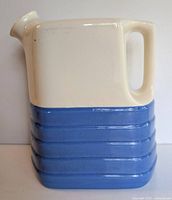 Side view showing two-tone coloring, handle, and narrow spout of rectangular jug with horizontal ribbing on bottom half.