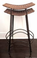 Front angled view of two wicker barstools stacked showing curved woven rattan seats and thin black metal frames with footrest bars.