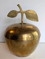 Front view of the brass apple dish showing smooth rounded form and stem with two leaves on lid.