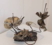Front angle view of Brutalist torch cut floral metal sculpture with stone base, showing details of petals and stems.