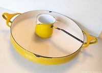 Overall view of yellow skillet and matching small creamer pot on white surface