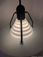 Close-up of the black metal frame holding the frosted stepped glass shade, showing the tiered concentric rings on the glass surface and the arm mounting point.