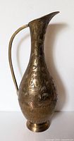 Front left side view of the etched brass vase showing details of the handle, neck, and floral engravings.