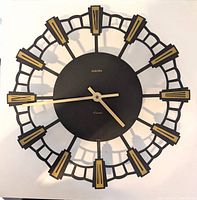Full view of the vintage Europa wall clock showing black and gold open lattice design with Roman numerals and clock hands.