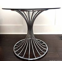 Side profile of chrome wire base and round glass top on dark wood floor