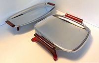 Front angled view of one oblong platter and one rectangular platter with wooden handles and feet