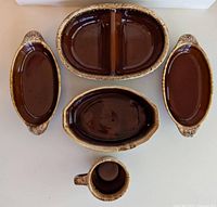 Top down view of five vintage Hull Pottery pieces including large divided dish, two handled oval dishes, smaller oval dish, and a mug.