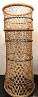Full view of tall rattan plant stand showing cylindrical shape and lattice weave.
