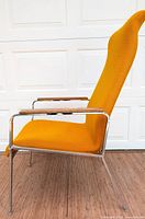 Side profile of mid-century lounge chair showing bright orange fabric, chrome frame, and wooden armrest.