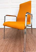 Front view of mid century lounge chair showing orange fabric upholstery, chrome frame, and wooden armrests.