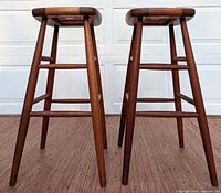 Full front view of the two wooden Mid Century style barstools showing their legs and base structure.