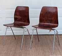 Front view of both chairs showing bent plywood seats and chrome legs on wooden floor with white garage door backdrop