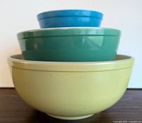 Three vintage Pyrex nesting bowls stacked with the yellow bowl at the base, green in the middle, and blue smallest bowl on top.