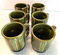 Overview of six green ceramic mugs with vertical ribbed texture and handles arranged in two rows.