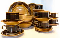 Set of stacked brown and mustard ceramic plates, bowls, cups, and saucers.