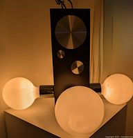 Front view of the space age chandelier showing three large frosted globe bulbs attached to a central black rectangular base with metallic round accents.