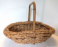 Side angle view of vintage woven basket showing braided body and handle.