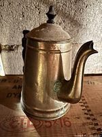 Side view of vintage metal teapot showing hinged lid with black finial, curved spout, and black handle attached with metal mounts.
