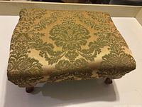 Top view of the footstool showing the ornate green damask fabric on beige background upholstery.