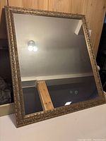 Front angled view of large rectangular gold framed mirror showing ornate carved detailing on the frame and clear reflective surface.