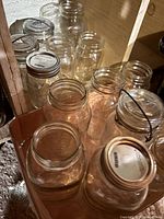 Various clear glass canning jars of assorted sizes with metal screw tops, arranged together on a wooden surface with some jars having rounded and some more cylindrical shapes.