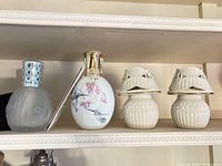 Photo showing two oil diffusers and two ceramic tea candle pots on a shelf