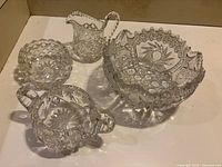 Photo showing four pieces of pinwheel crystal and glassware including a large bowl, creamer, sugar bowl, and round bowl with handles.