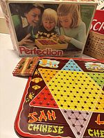 Photo of Perfection game box, Chinese Checkers board, and a wooden peg container
