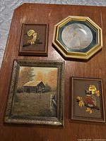 Four picture frames displayed on a wooden table: an octagonal gold-tone frame with woman's image, two brown wooden frames with embroidered owls, one bronze-tone frame with barn painting.