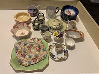 Overview of assorted vintage dishes arranged on table showing multiple plates, bowls, pitchers and decorative ceramics.
