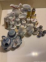 Top view showing arrangement of assorted salt and pepper shakers and ceramic dishware on a mirrored surface.