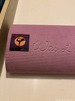 Close-up of pink textured yoga mat showing woven fabric patch with Wai Lana logo and embossed logo on mat surface.