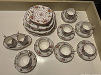 View of several teacups and saucers, creamer, and sugar bowl arranged together showing fine china with floral design and gold accents.