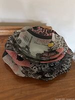 Stack of glass plates and bowls with Paris-themed design showing Eiffel Tower, Metro sign, and text in pink, black and beige colors, scalloped edges visible.
