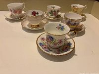 Full set of six vintage teacups with saucers displayed, showing diverse floral patterns and gold trim on each piece.
