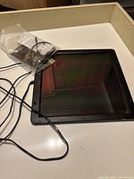 Small black framed solar panel on white surface with attached cable.