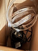 Photo showing a used black sump pump unit with clear flexible tubing and a power cord inside a cardboard box, showing some residue and signs of wear.