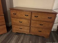 Front view of the brown wooden dresser showing six drawers with decorative metal handles and wood grain finish.