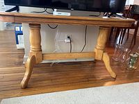 Full front view of the traditional wooden table showing the top and leg design, with TV stand on top and some glassware beside.