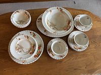 Full view of the dish set on a wooden table showing various plates, bowls, cups, and saucers with floral patterns.