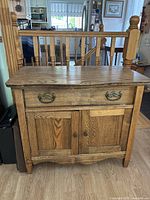Front view of vintage wood cabinet with drawer and double doors, brass handles, and visible wood grain.