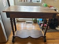 Full view of the brown wooden table with turned legs and lower shelf, showing vintage wooden construction and surface wear.