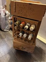 Front angled view of handmade wooden swivel paint organizer showing front panel with circular cutouts holding paint bottles, decorative cat and floral engravings, top tray, and drawer at bottom.