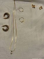 Photo showing gold-plated chain necklace with pearl pendant, two pairs of earrings (hoop and large clip-on), and an additional pair of small stud earrings