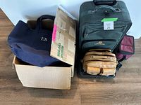 Photo showing the collection of travel bags and boxes including a large rolling suitcase, tote bag, leather shoulder bag, and small insulated lunch bag